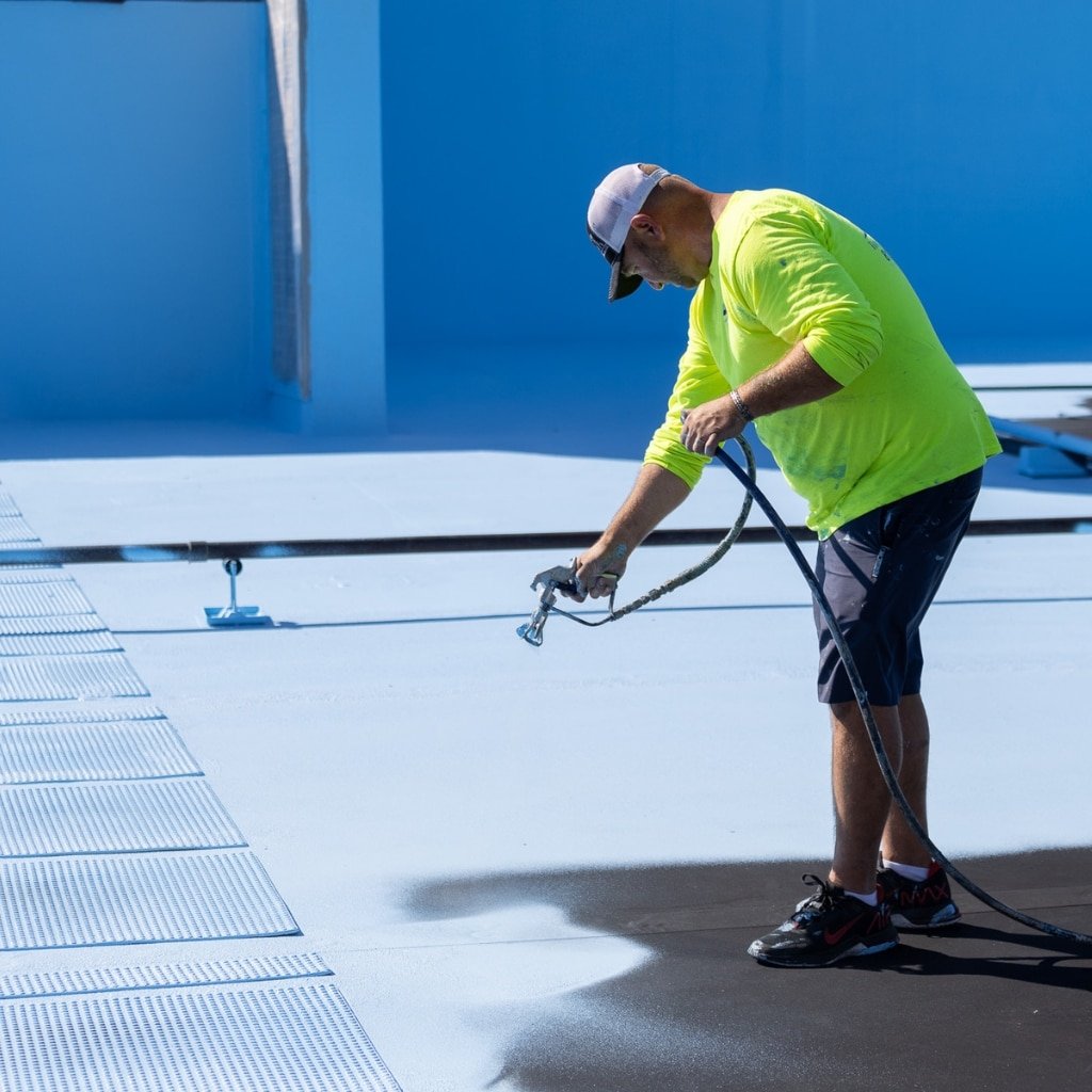 Technician applying elastomeric roofing material on a low-slope building